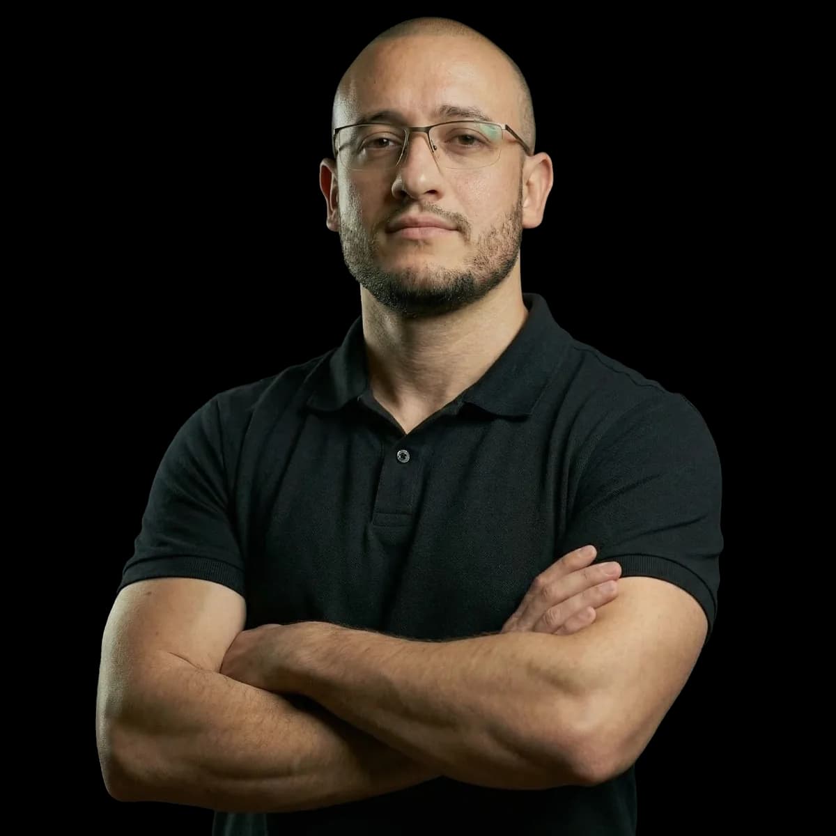 Cristiano Pereira with arms crossed, wearing glasses and a black polo shirt, looking at the camera